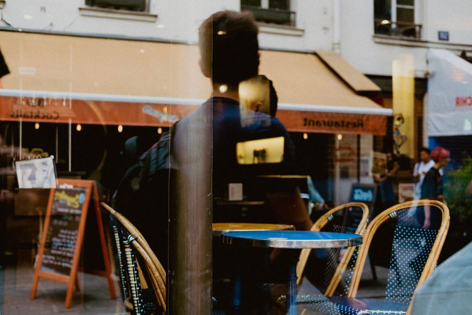 A dynamic urban scene capturing reflections in a café window with visible pedestrians and seating.